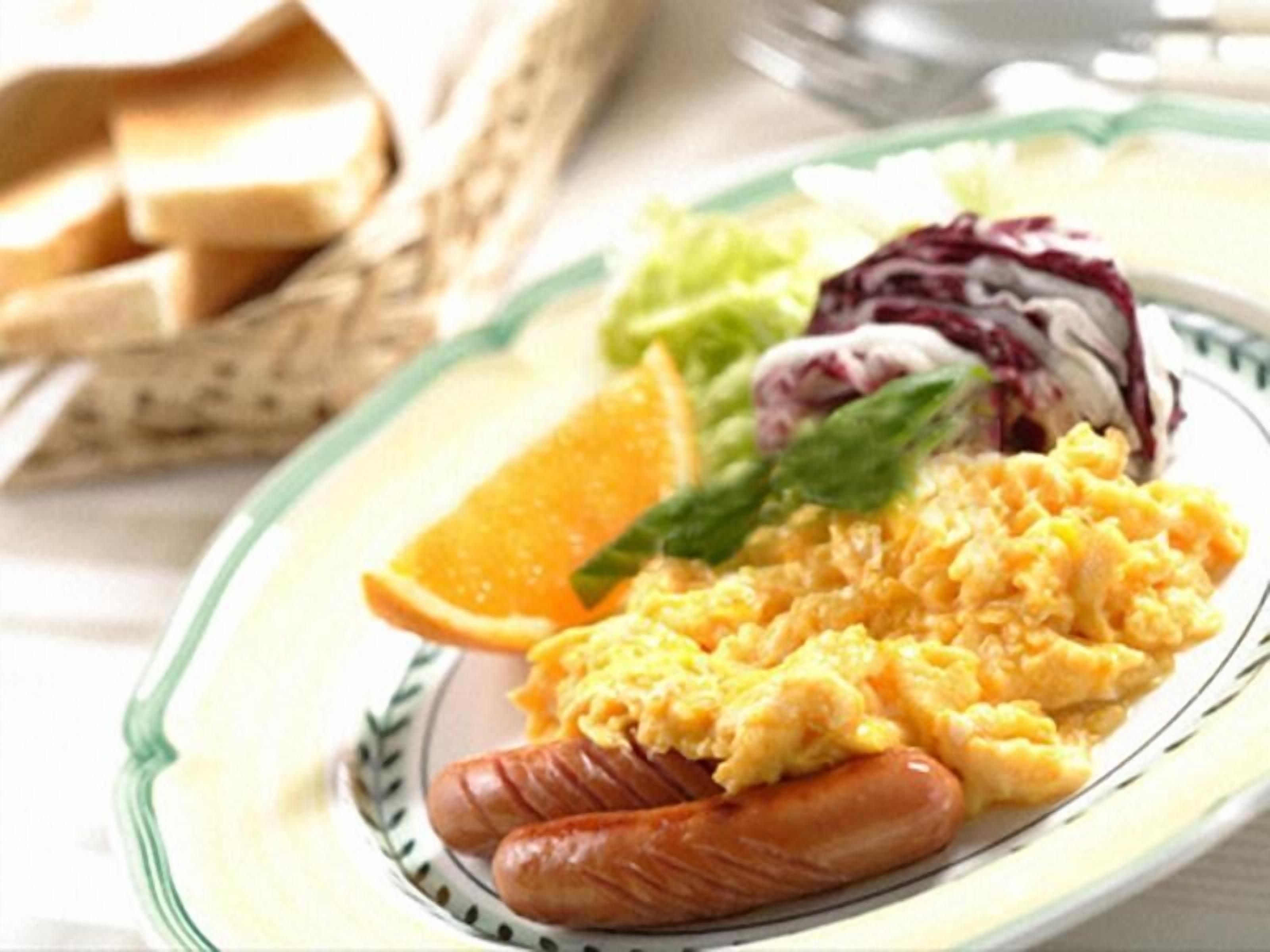 A plate with scrambled eggs, sausage, a slice of orange, and a side salad.