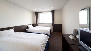 A hotel room with two beds, a television, and a window with curtains.