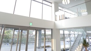 A spacious lobby with a high ceiling, large windows, and a staircase leading to an upper level.