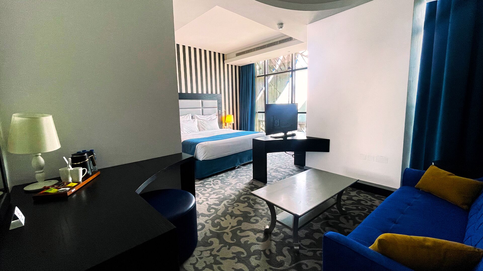 A hotel room with a bed, a desk, a chair, a sofa, and a TV.