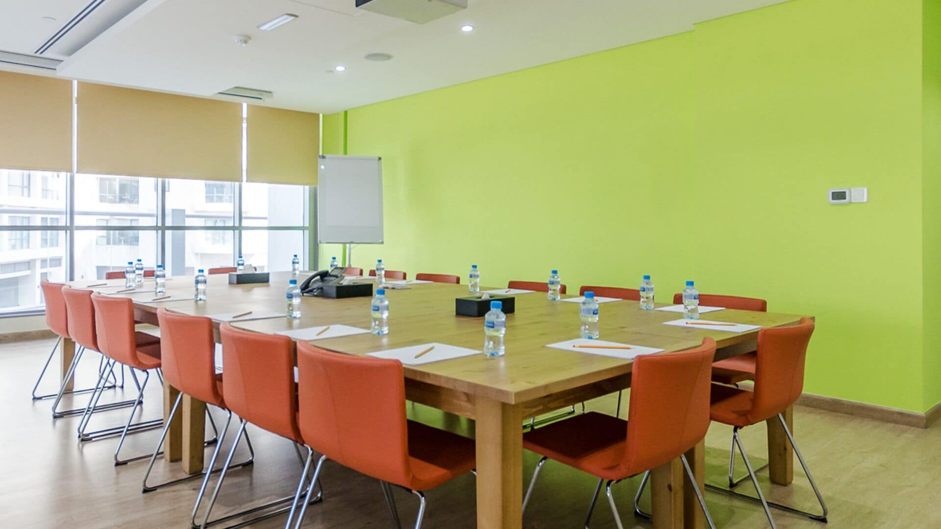 A conference room with a long table, orange chairs, water bottles, and a whiteboard.