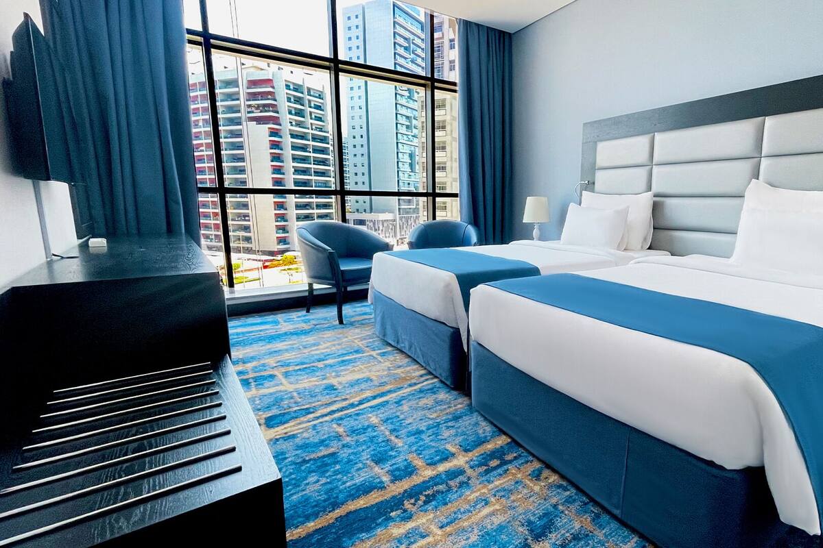 A hotel room with a large window, two beds, a desk, and a chair.