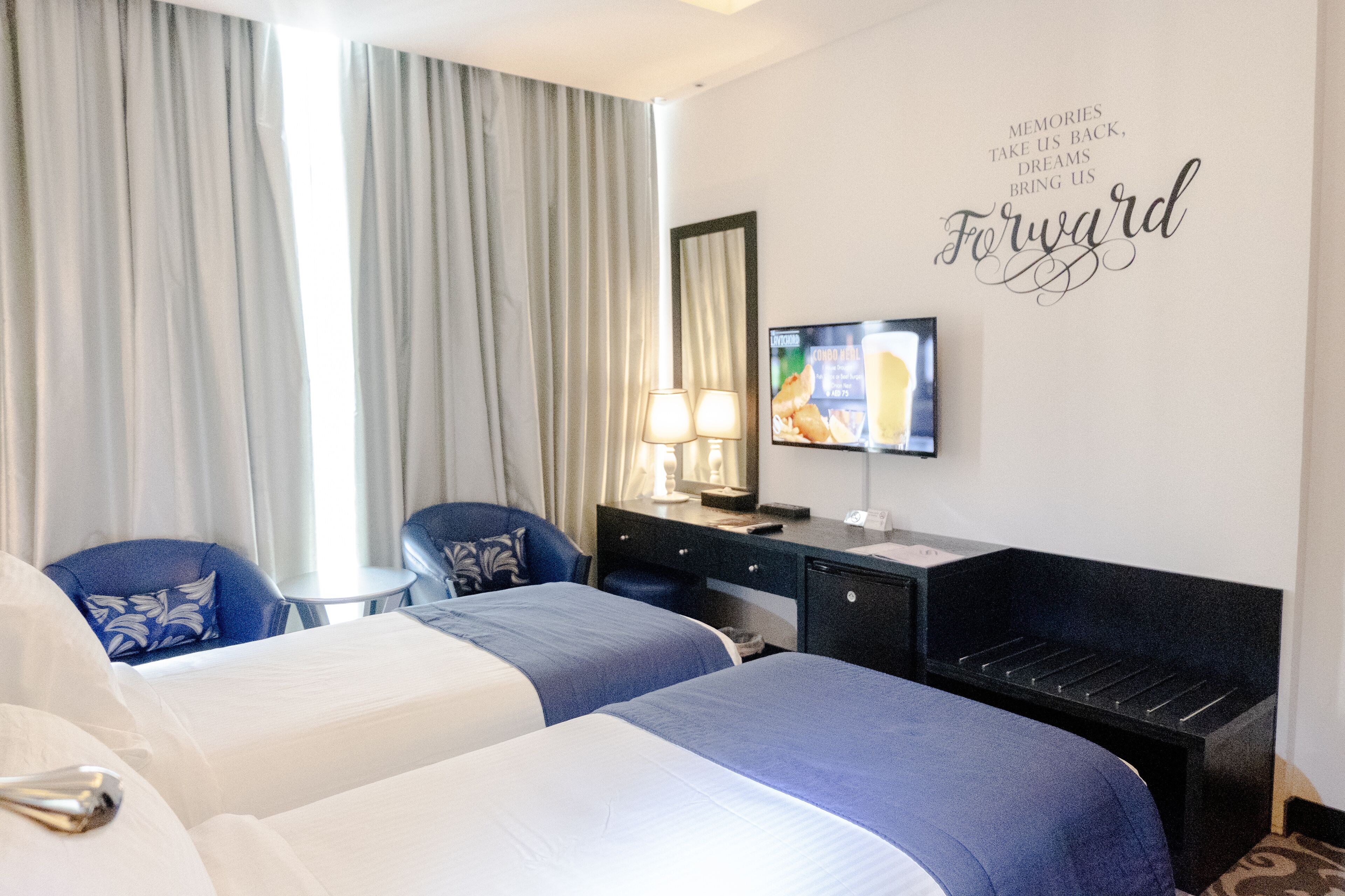 A hotel room with two beds, a desk, a chair, a television, and a wall with a motivational quote.