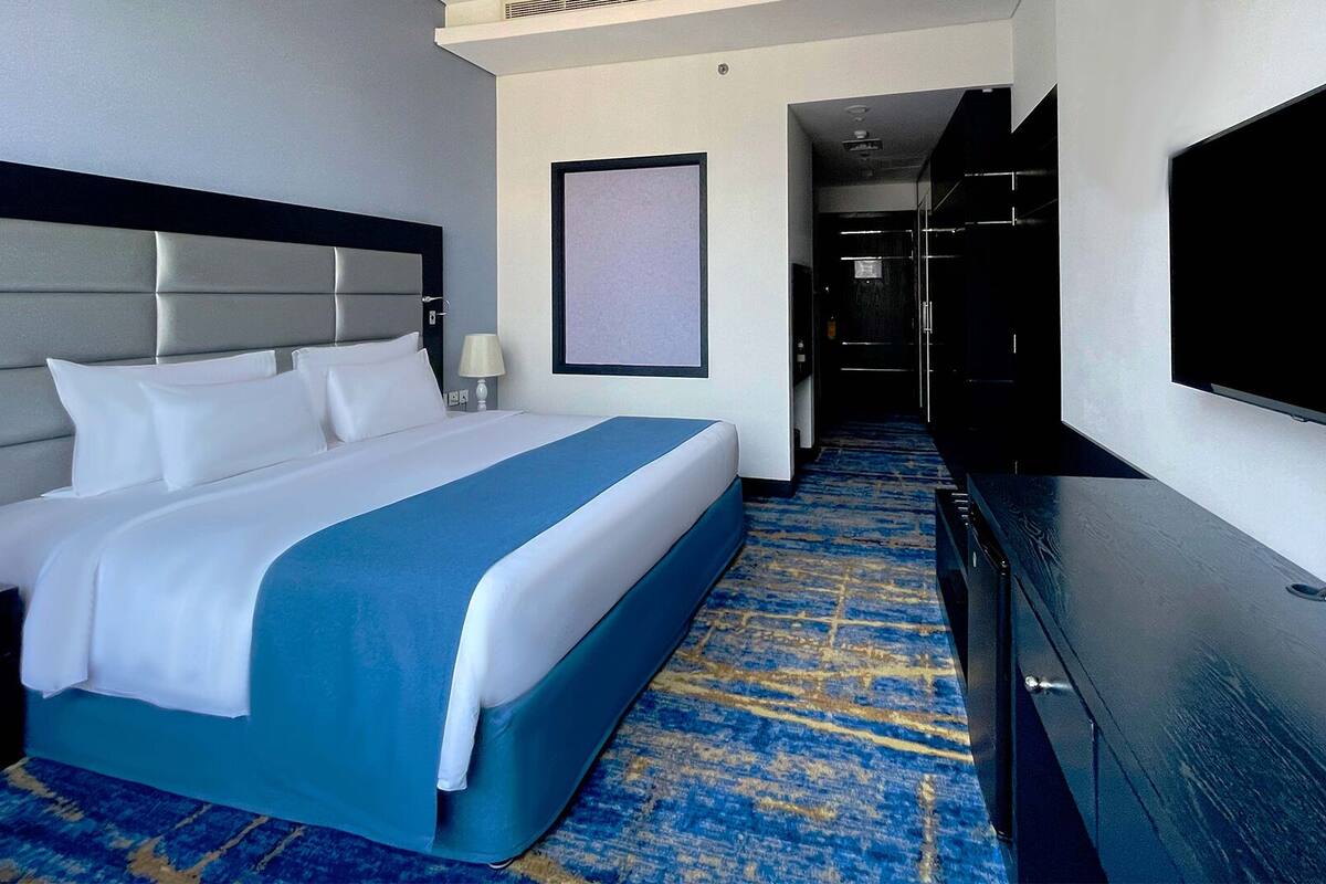 A hotel room with a large bed, a flat-screen TV, a desk, and a carpeted floor.