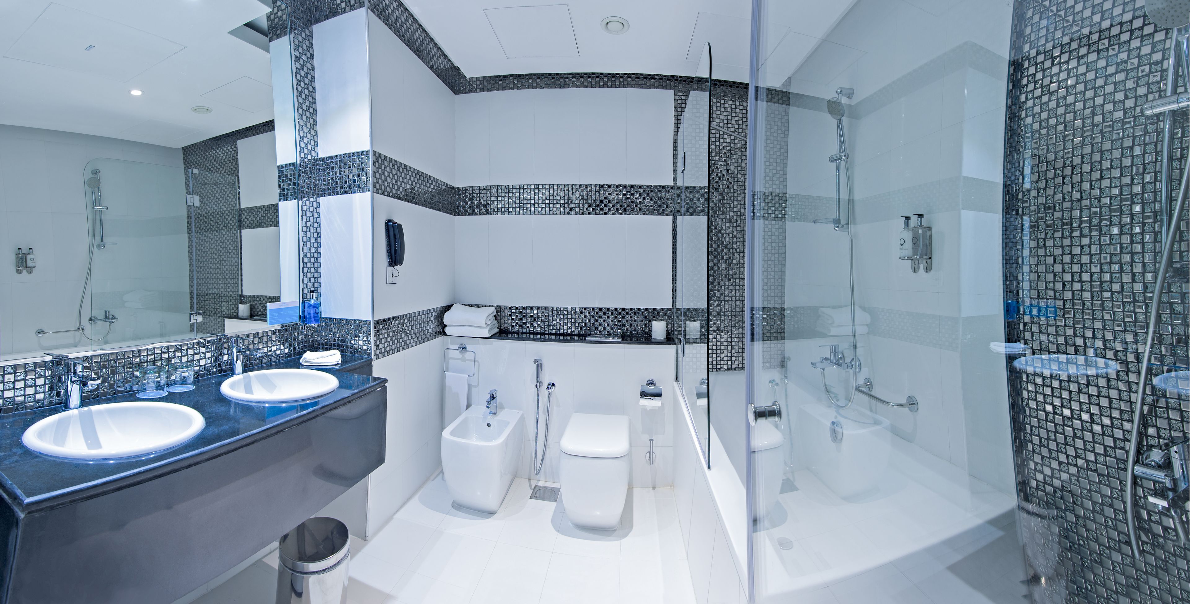 A modern bathroom with two sinks, a bidet, a toilet, and a glass-enclosed shower area.
