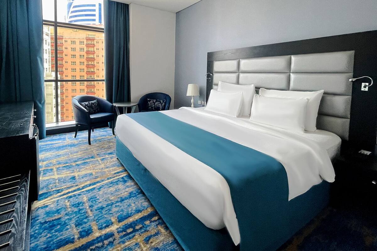 A hotel room with a bed, a desk, a chair, a TV, and a window with a view of buildings.