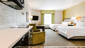 Habitación de hotel con cama, escritorio, silla, televisión y ventana con cortinas.