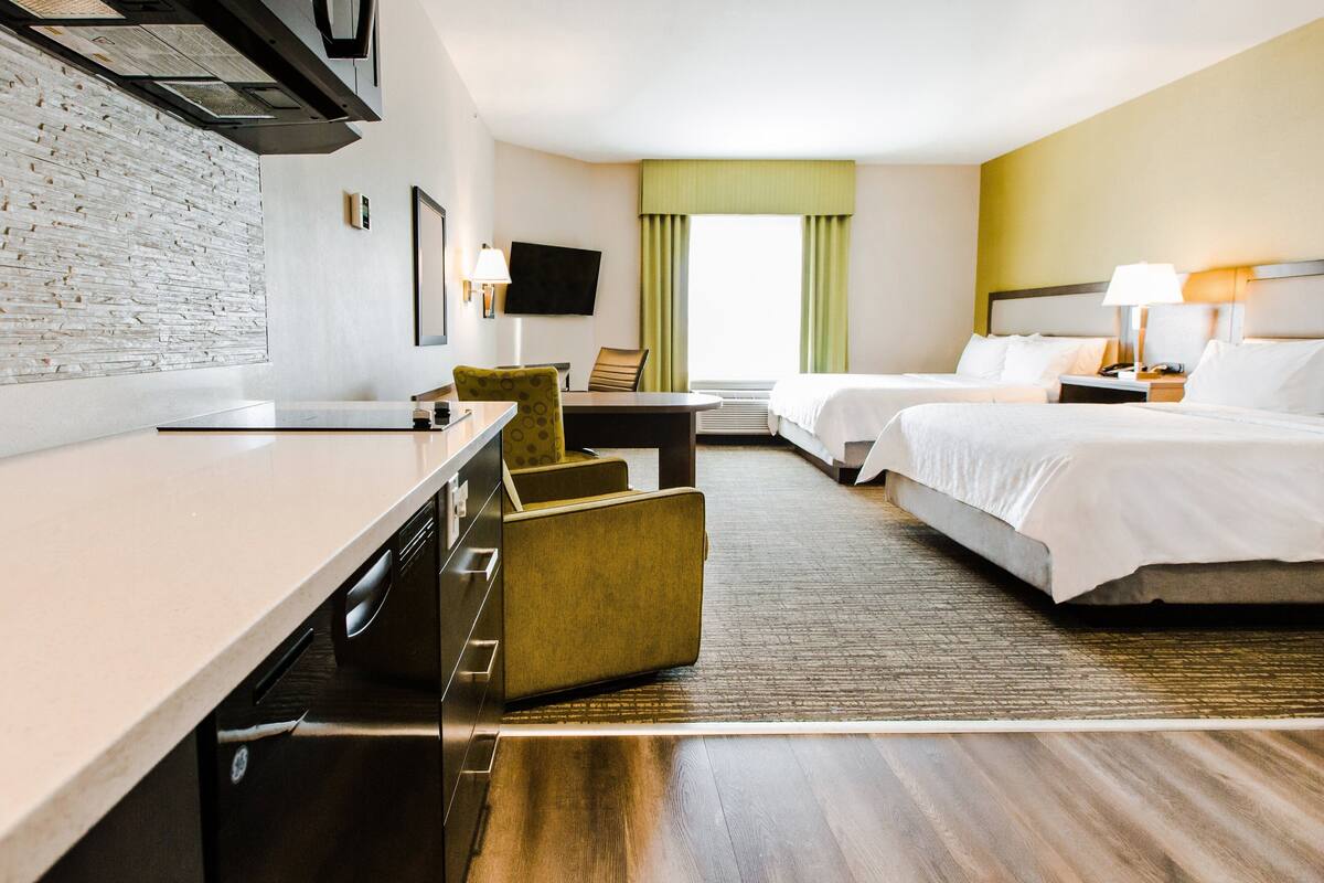 Habitación de hotel con cama, escritorio, silla, televisión y ventana con cortinas.