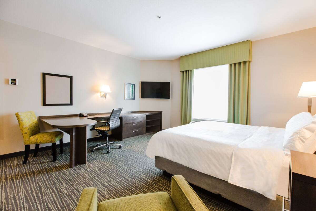 Habitación de hotel con cama, escritorio, silla, televisor y ventana con cortinas.