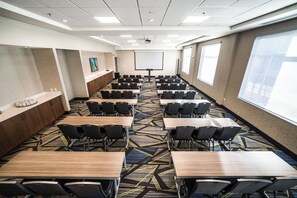 Un salón de conferencias con varias mesas y sillas, una pizarra y una pantalla para proyector.