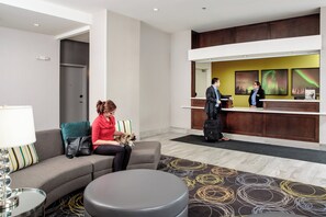 A hotel lobby with a reception desk, a sofa, a coffee table, and a patterned rug.