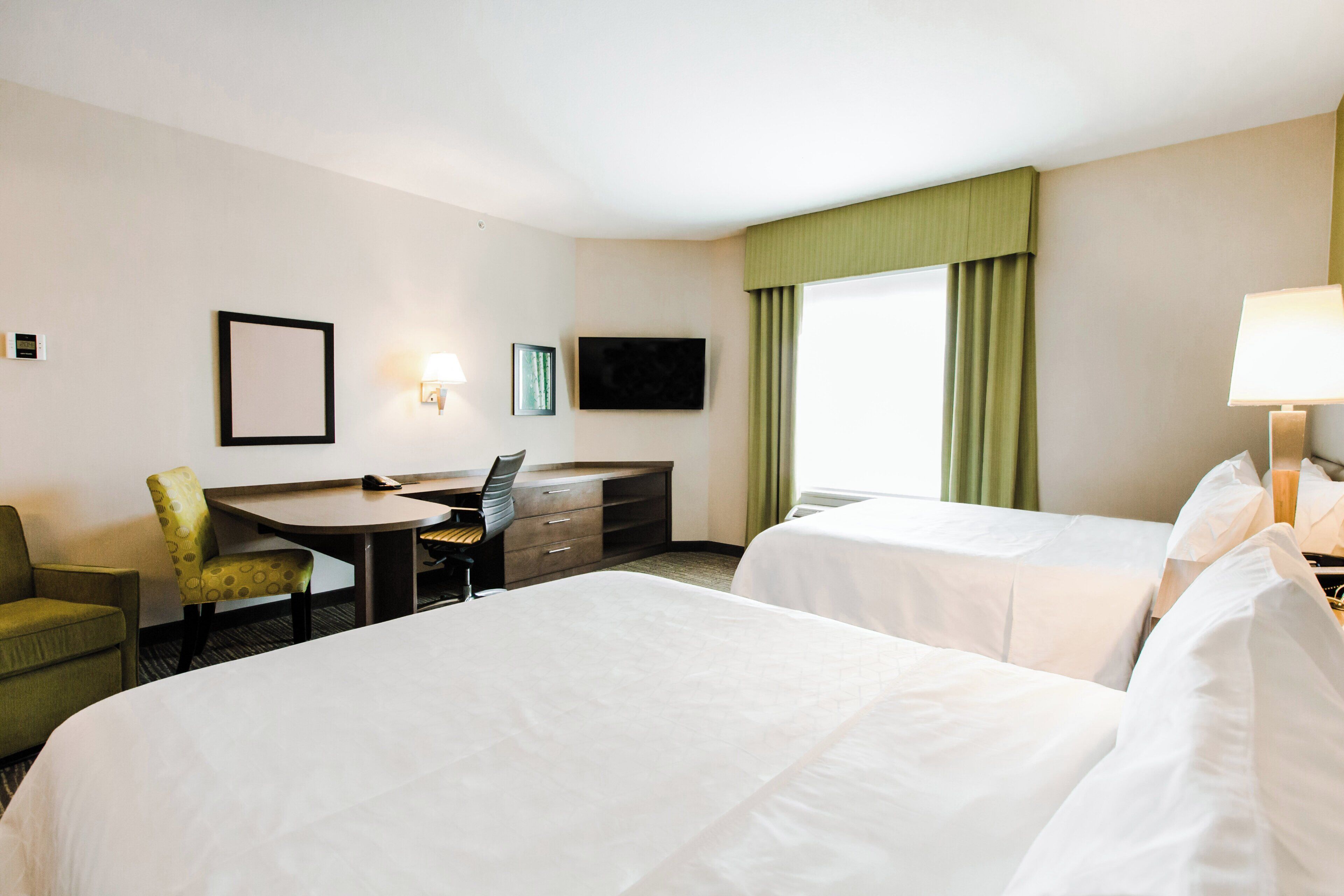 A hotel room with two beds, a desk, a chair, a TV, and a window with curtains.