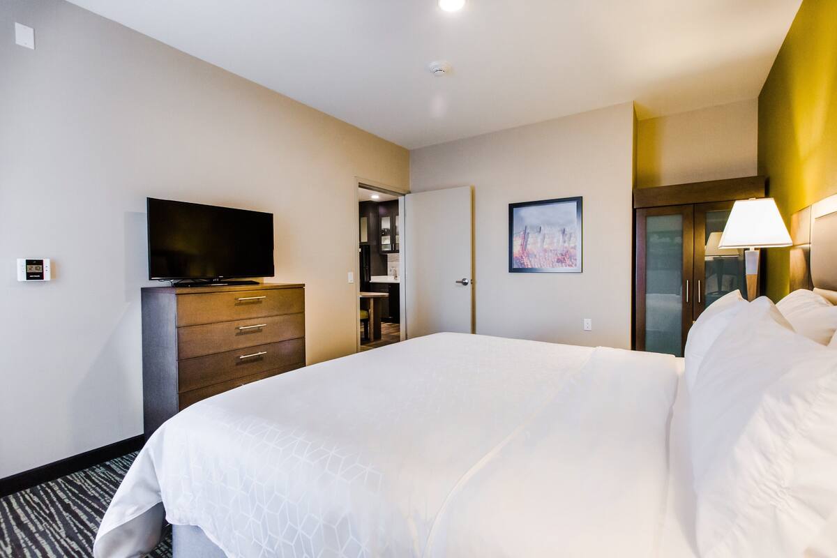 Habitación de hotel con una cama grande, un televisor de pantalla plana, un aparador, una puerta que da al baño y un cuadro en la pared.