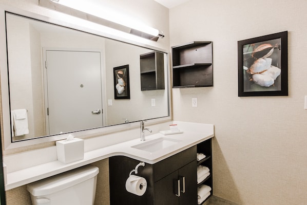 Un baño moderno con un espejo grande, un lavabo blanco, armarios oscuros y un cuadro enmarcado en la pared.
