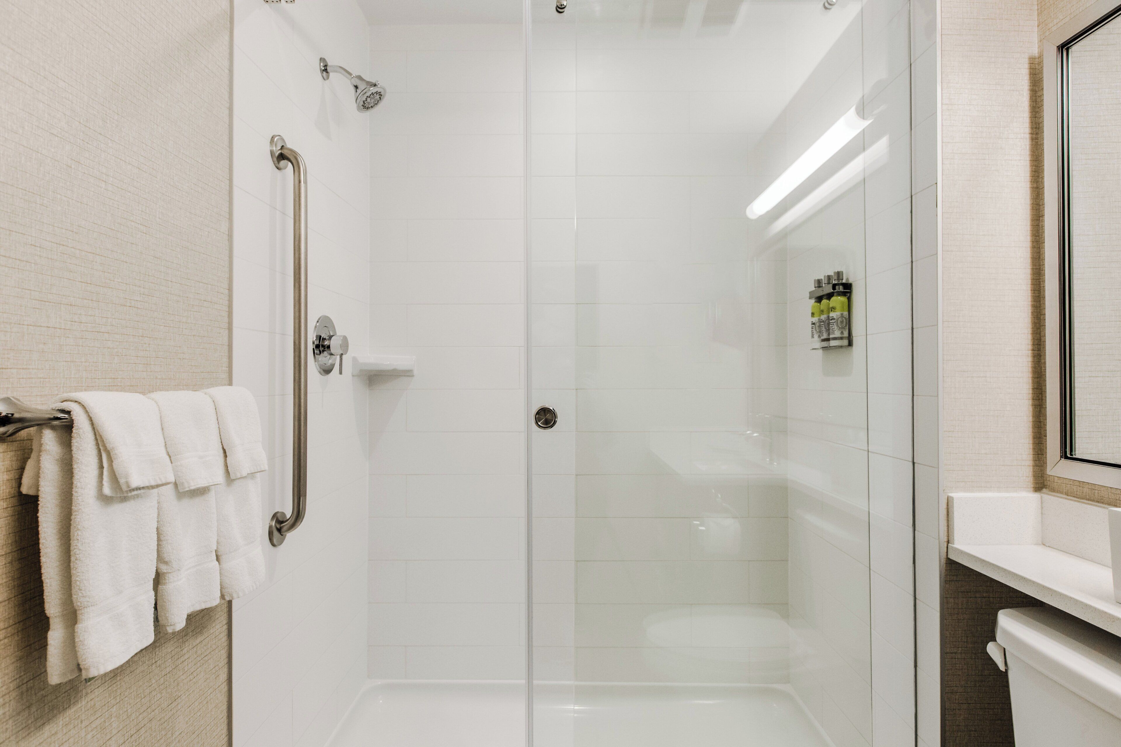 A modern bathroom with a glass-enclosed shower, a white tiled wall, and a visible toilet.