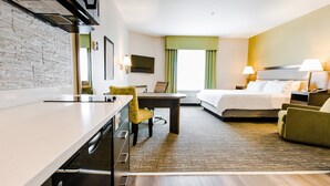 Una habitación de hotel con cama, escritorio, silla, televisor y ventana con cortinas.