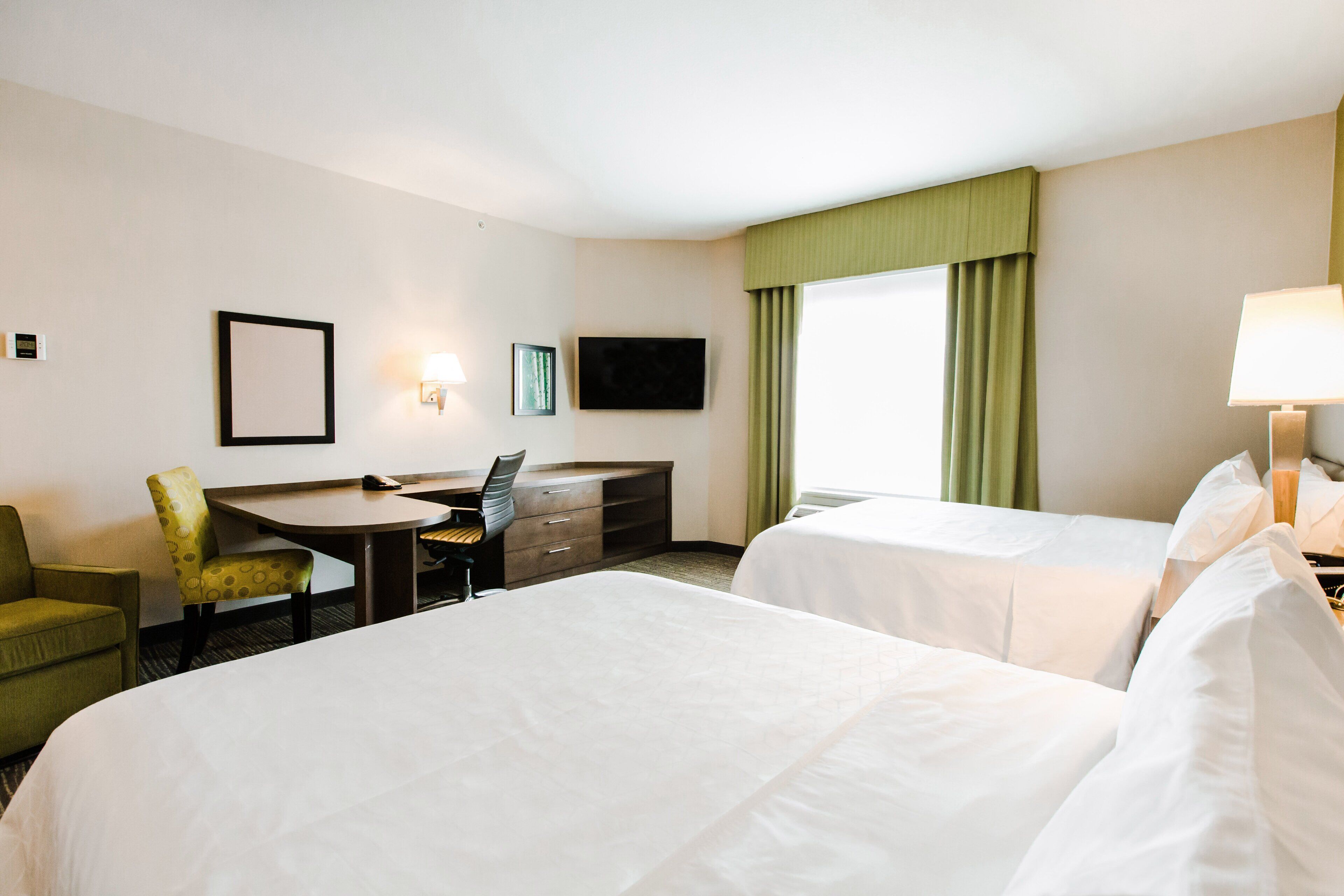 Een hotelkamer met twee bedden, een bureau met stoel, een televisie en een raam met gordijnen.