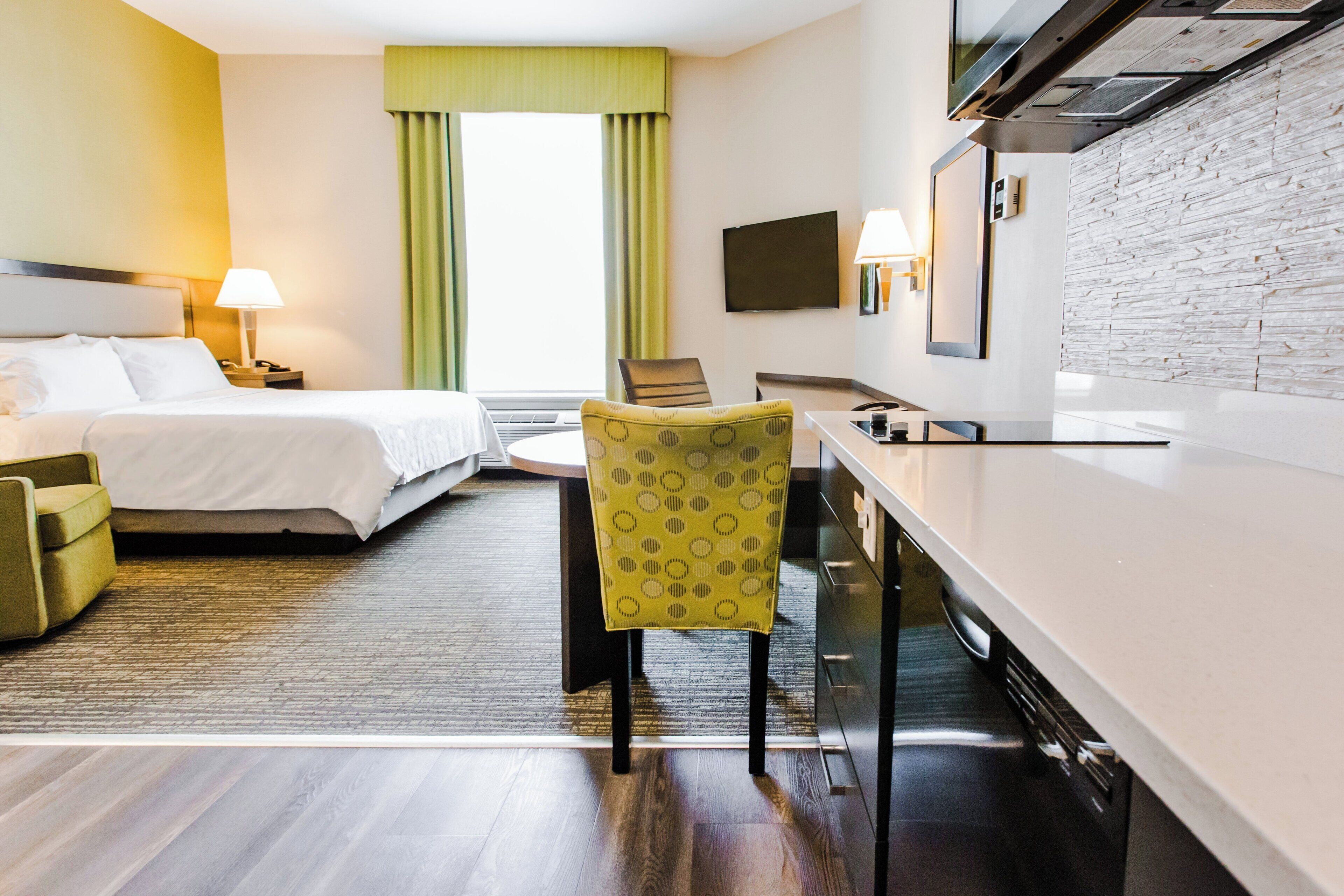 A hotel room with a bed, a desk, a chair, a TV, and a stone wall.