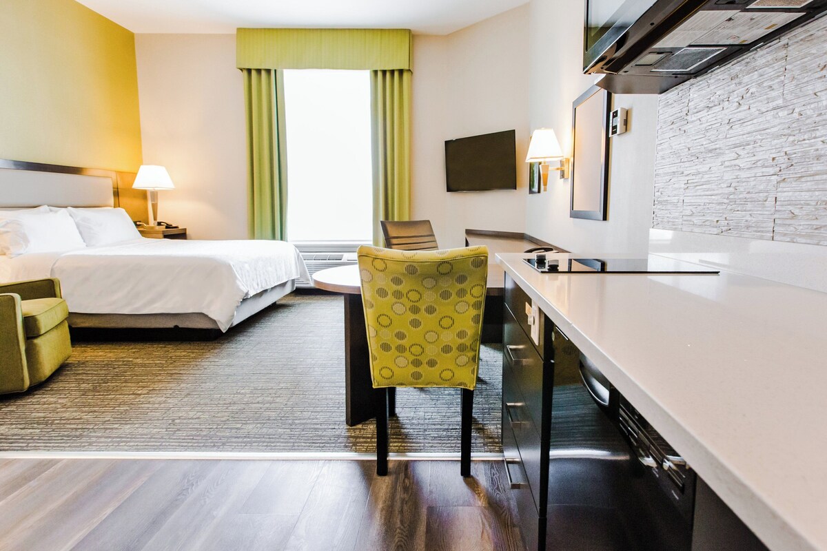 Quarto de hotel com cama, escrivaninha, cadeira, televisão e parede de pedra.