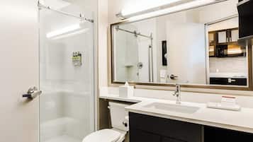 A modern bathroom with a glass shower enclosure, a white toilet, a sink with a mirror above it, and a black cabinet below.