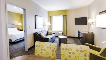 A hotel room with a bed, a sofa, a dining table, and a TV.