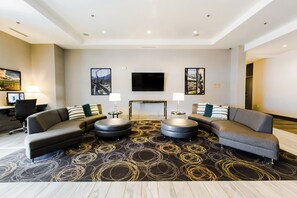 Eine moderne Hotelhalle mit einer Eckcouch, zwei runden Hocker, einem Flachbildfernseher und Kunstwerken an den Wänden.