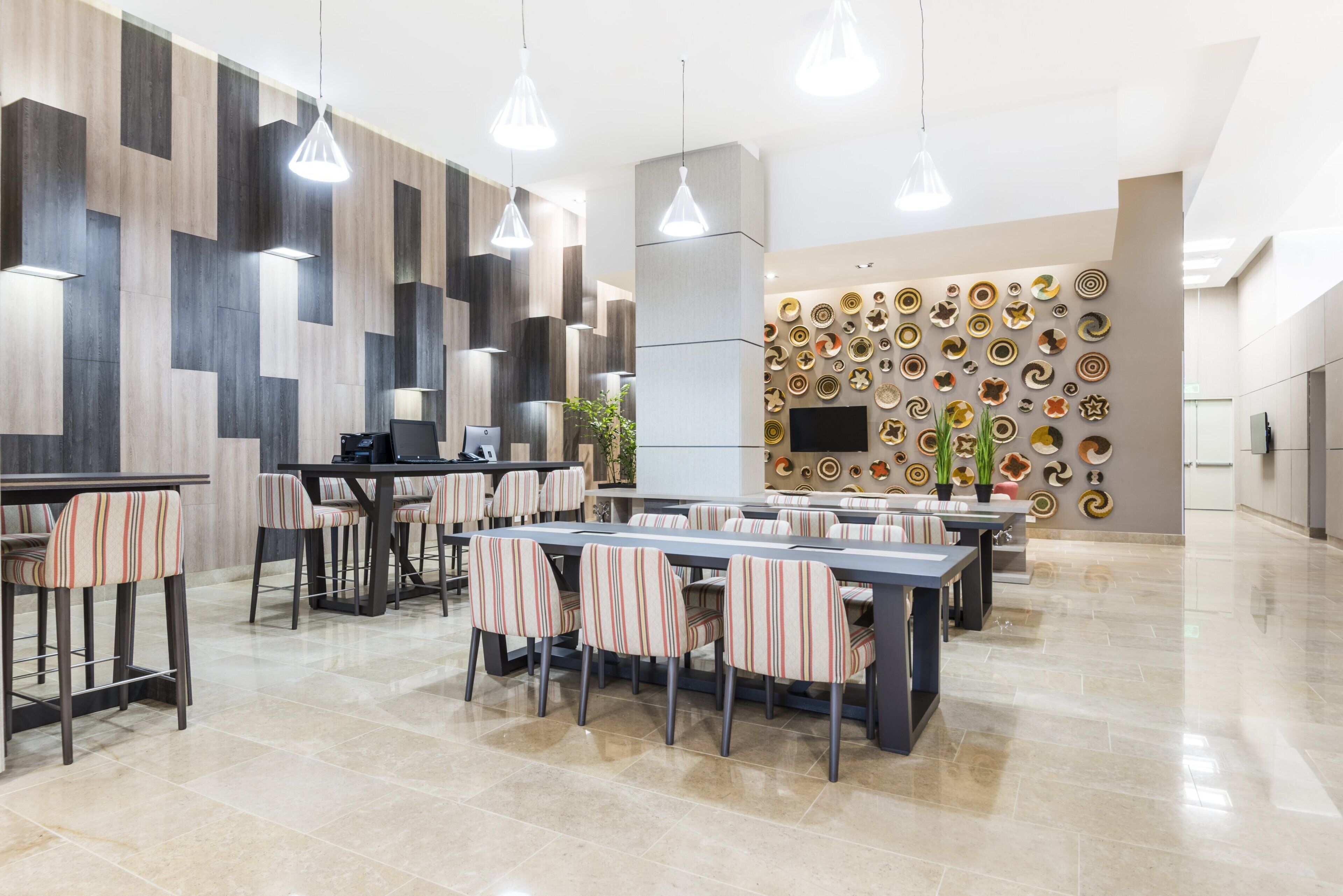 A modern hotel lobby with a long reception desk, multiple seating areas, and a wall decorated with circular art pieces.