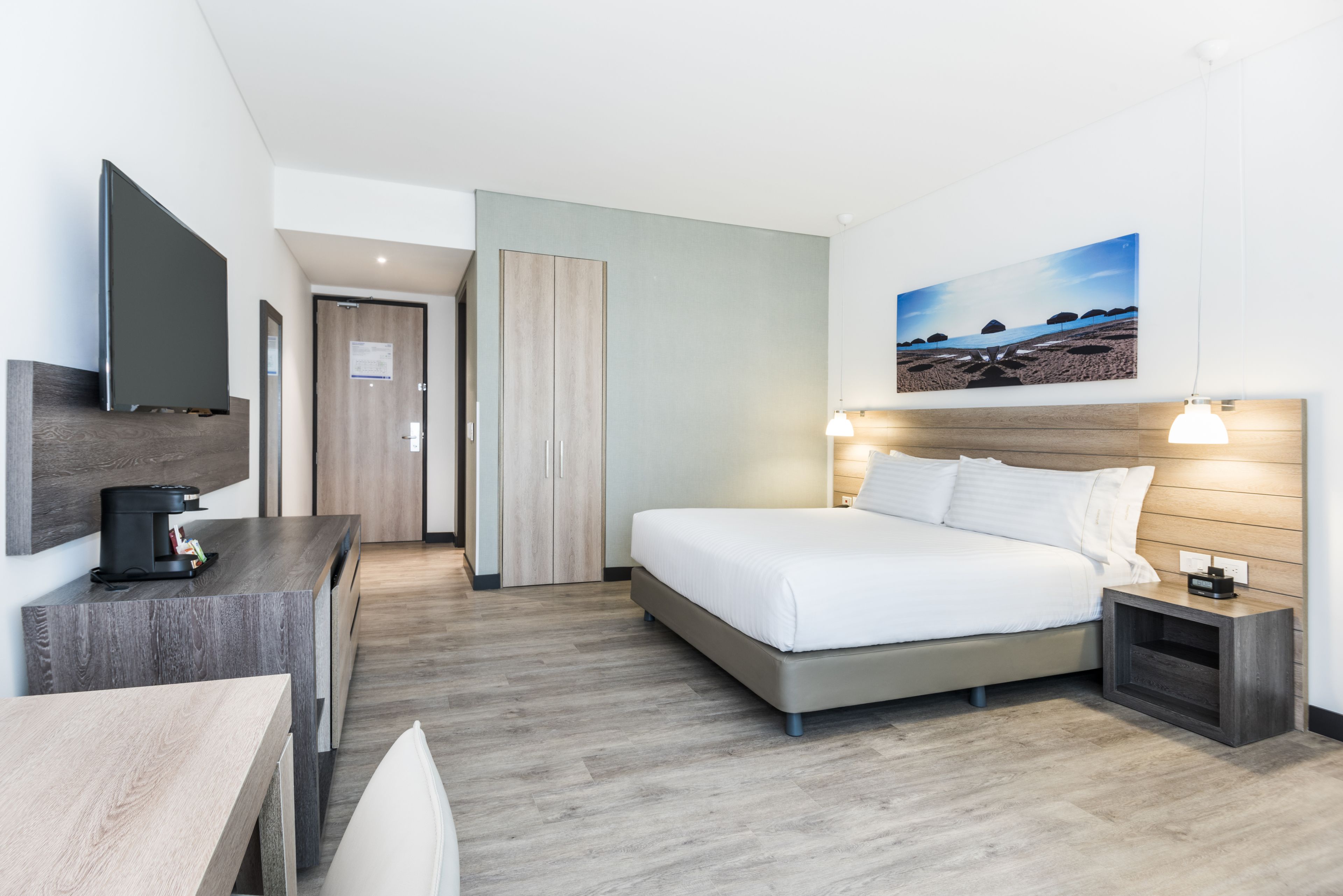 Ein modernes Hotelzimmer mit Bett, Nachttisch und einem wandmontierten Flachbildfernseher.