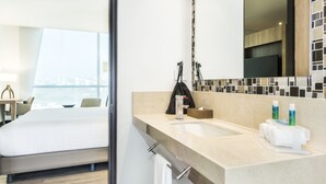 A modern hotel room with a large bed, a bathroom with a sink, and a view of the city. - Holiday Inn Express Barranquilla Buenavista by IHG (Barranquilla)