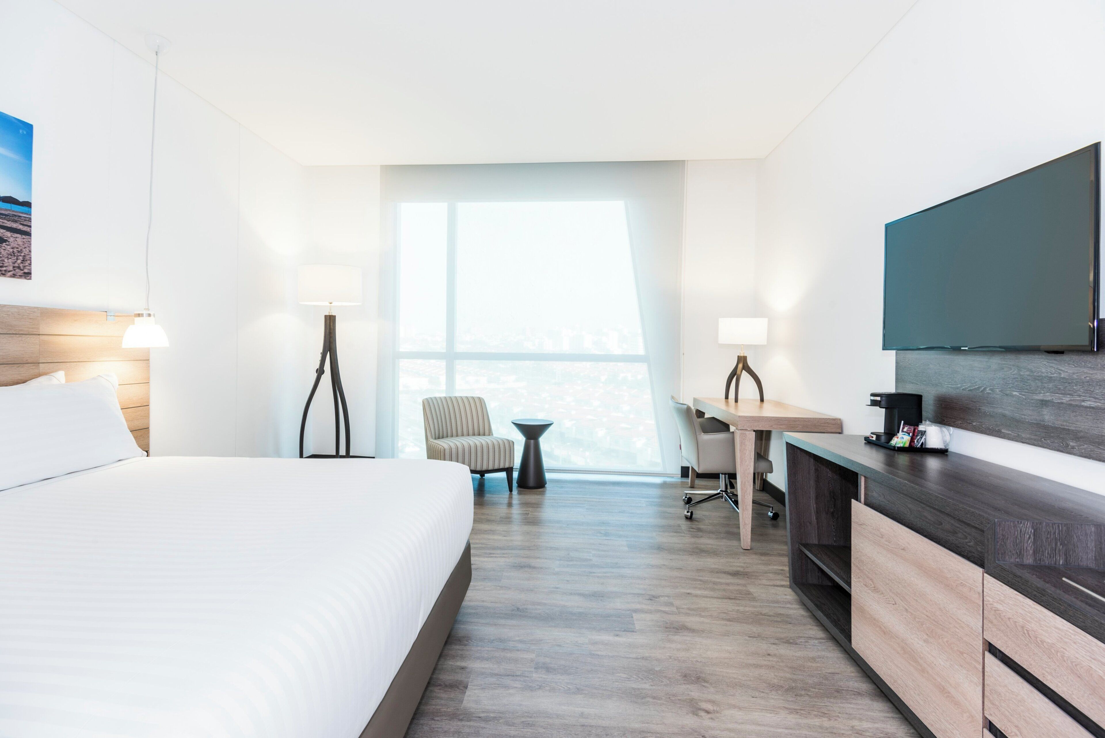 A hotel room with a bed, desk, chair, and a large window.
