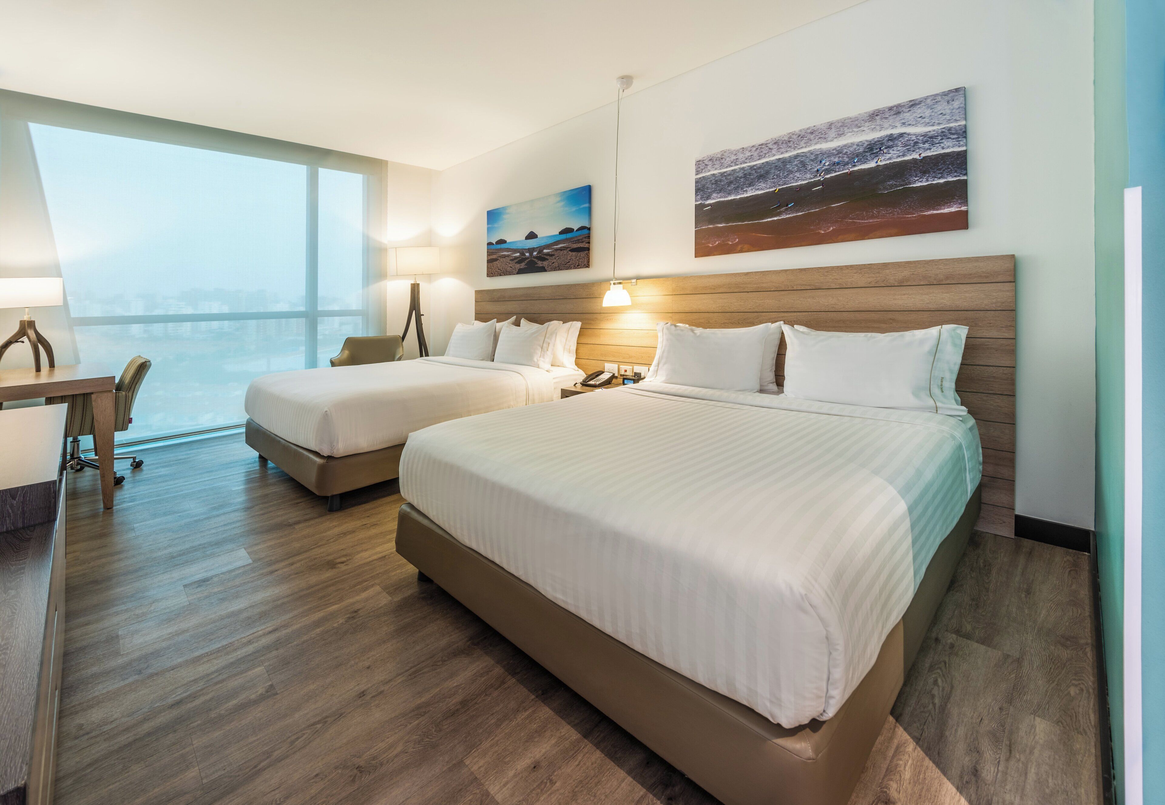 A hotel room with two beds, a desk, and a large window.