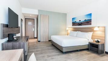 Habitación de hotel con cama, mesita de noche, televisión y un cuadro de una playa.