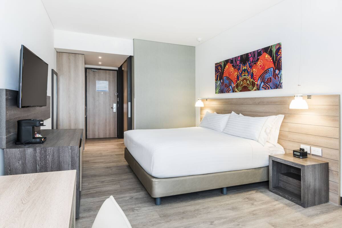 Ein modernes Hotelzimmer mit einem Bett, einem Nachttisch und einem Flachbildfernseher auf einer Kommode.