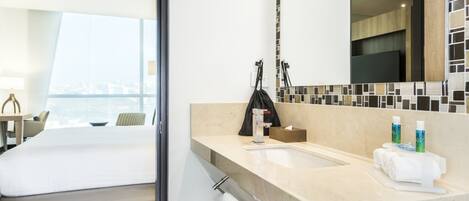 A hotel room with a bed, a bathroom with a sink, a mirror, and toiletries.