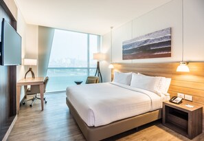 Ein modernes Hotelzimmer mit einem großen Bett, einem Schreibtisch, einem Sessel, einem Fernseher, einer Lampe und einem Bild an der Wand.