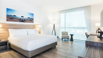 Una habitación de hotel con cama, escritorio, silla, lámpara y un ventanal grande.