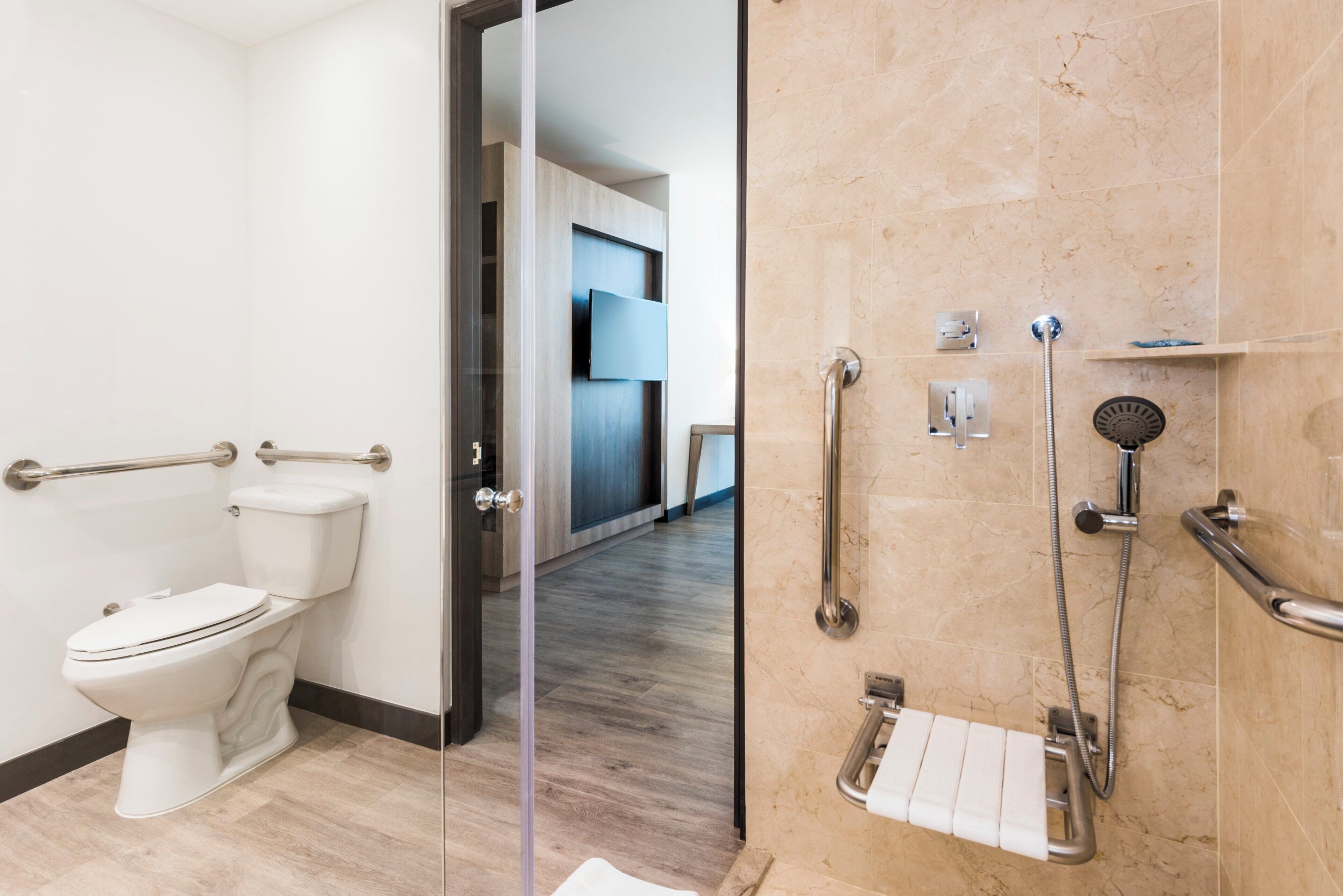 A modern bathroom with a toilet, a shower with grab bars, and a glass partition.