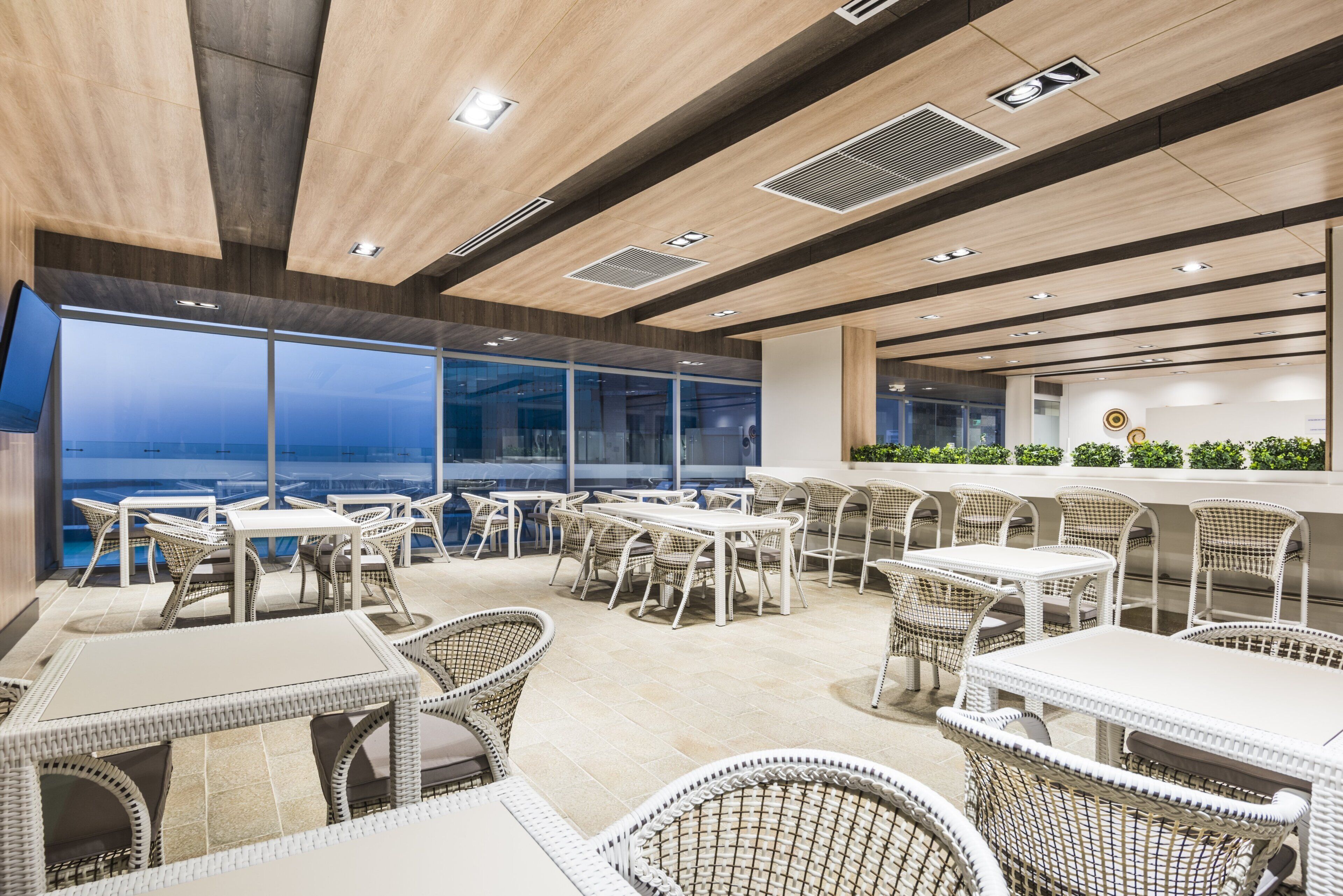 A modern outdoor dining area with wicker furniture and large windows overlooking the sea.