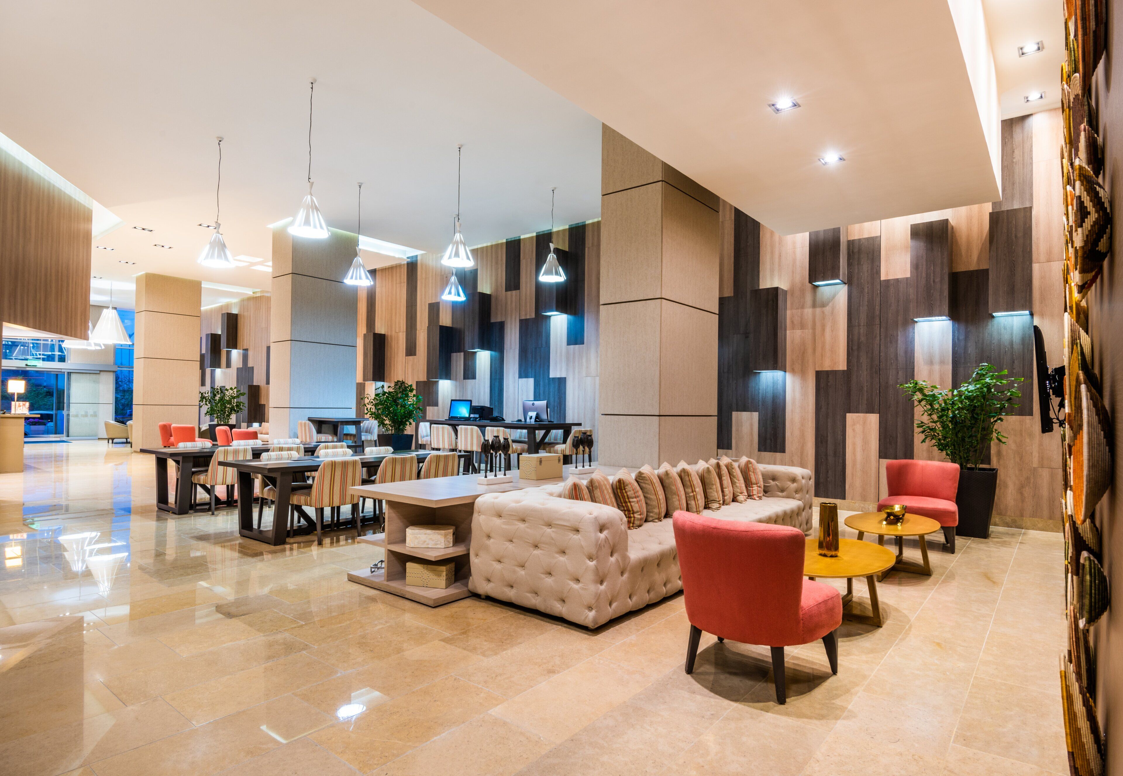 A modern hotel lobby with a seating area, tables, and a bar.