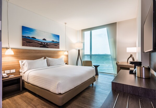 Ein Hotelzimmer mit einem großen Bett, einem Schreibtisch, einem Sessel, einem Fernseher und einem Gemälde an der Wand.