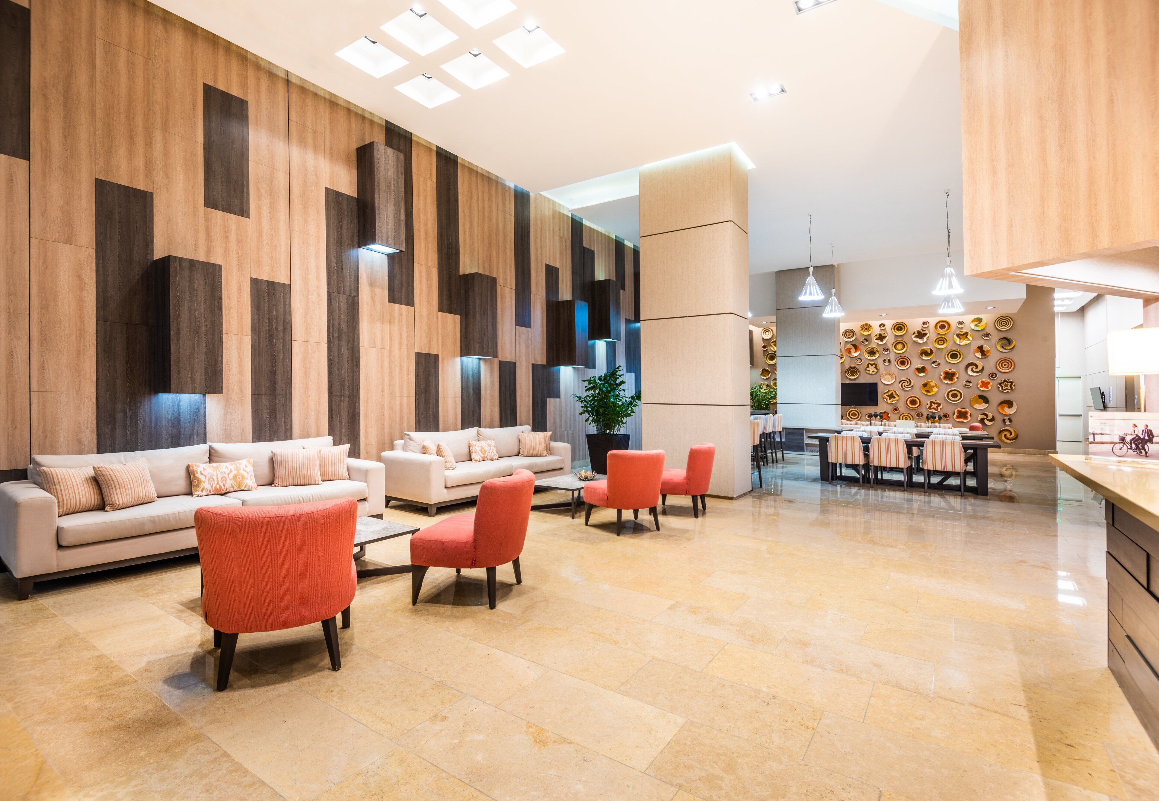A modern hotel lobby with a seating area, a dining space, and a wall with decorative plates.