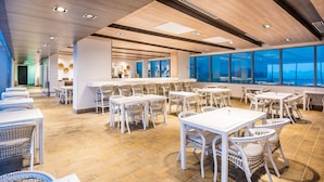 Un vaste espace de restauration intérieur, doté de nombreuses tables et chaises, de grandes fenêtres offrant une vue dégagée et d’un design moderne au niveau du plafond.