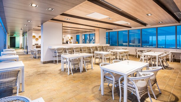 A spacious indoor dining area with multiple tables and chairs, large windows offering a view, and a modern ceiling design. - Holiday Inn Express Barranquilla Buenavista by IHG (Barranquilla)