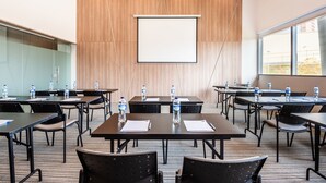 Une salle de conférence équipée de tables, de chaises, d’un écran de projection et de bouteilles d’eau.