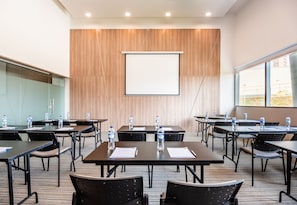 Un salón de conferencias con mesas, sillas, una pantalla de proyector y botellas de agua.