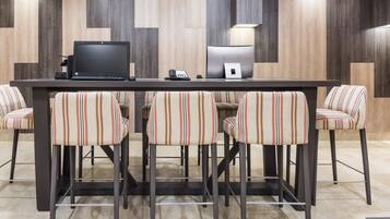 A modern bar area with a long table, four striped bar stools, a laptop, a telephone, and a small lamp.