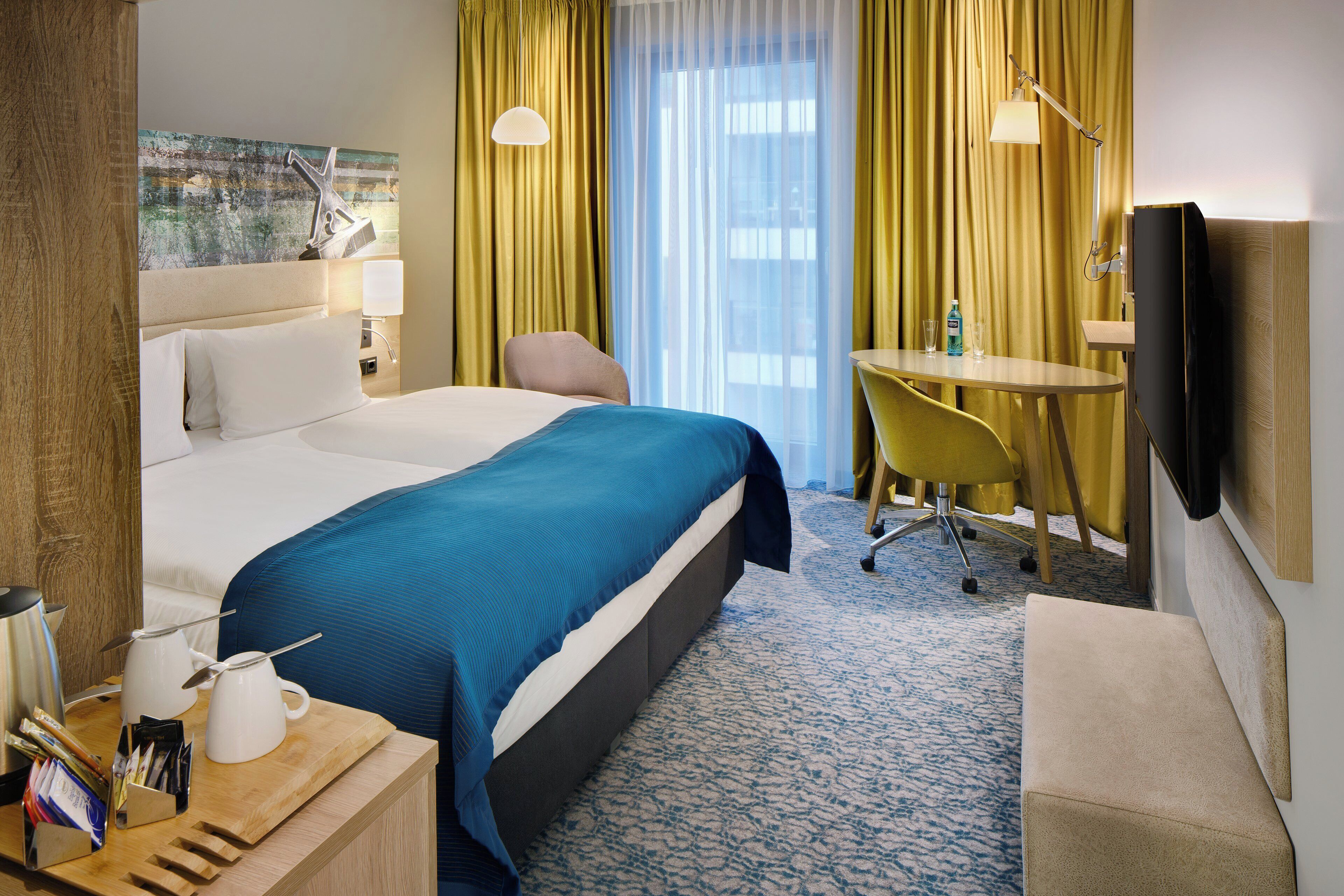 Een hotelkamer met een groot bed, een bureau met stoel, een televisie en een raam met gordijnen.