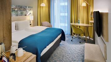 Een hotelkamer met een groot bed, een bureau met stoel, een televisie en een raam met gordijnen.