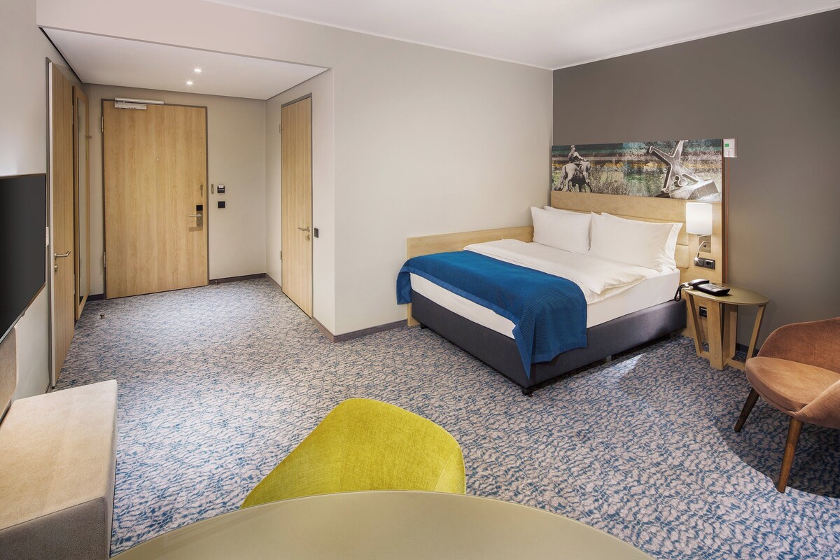 Una habitación de hotel con una cama, un escritorio, una silla y un cuadro en la pared.