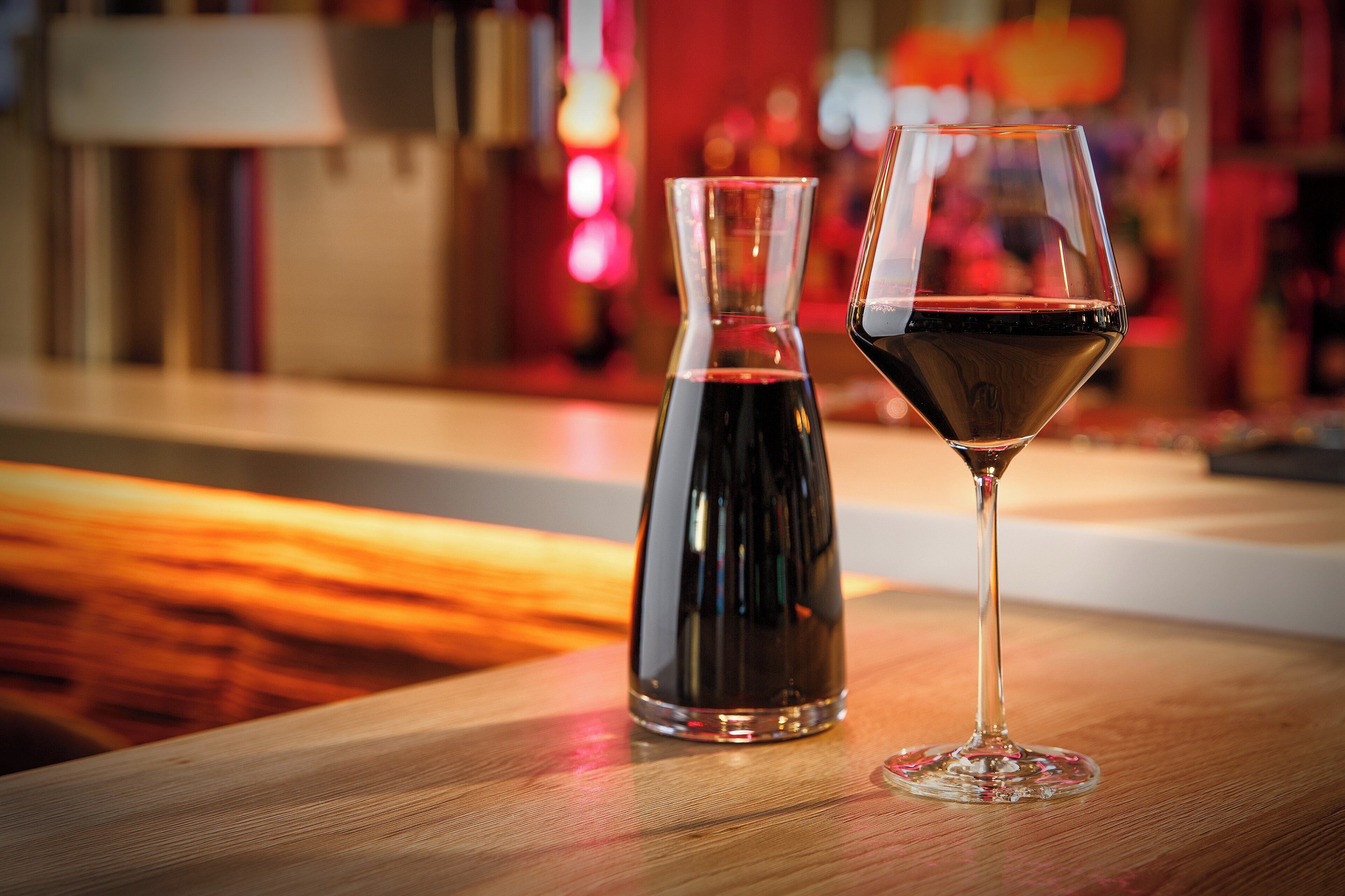Ein Glas Rotwein und eine Karaffe auf einer Holztischplatte.
